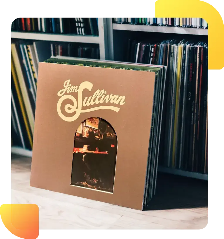 A vinyl record with a brown cover featuring the name 'Jim Sullivan' in large, stylized white letters at the top. Below the name, there is an arched window cutout revealing part of an image inside of a dimly lit room with furniture. The record is standing upright in front of a shelf filled with a collection of other vinyl records.